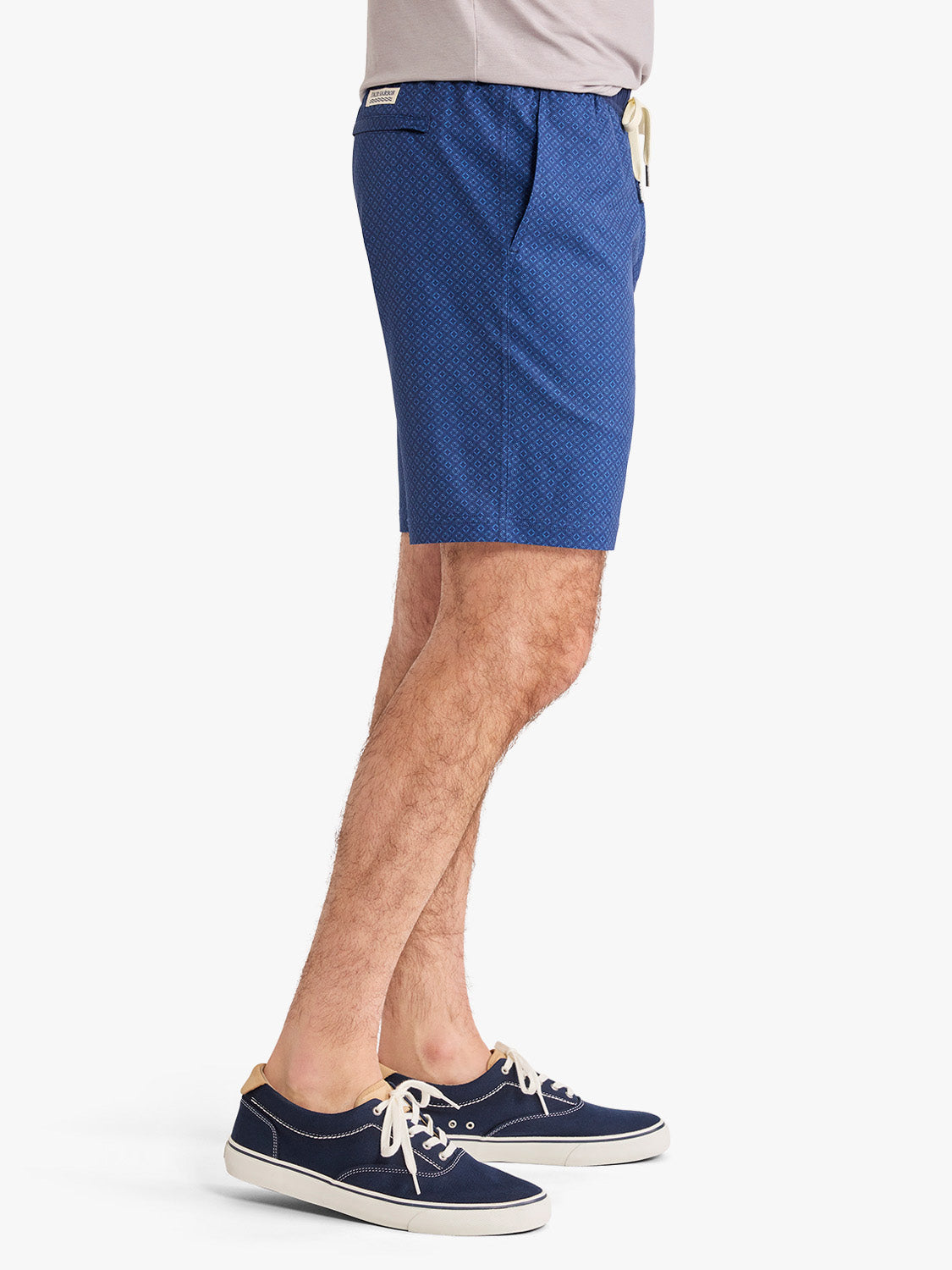 Man wearing blue shorts with small circle pattern and navy canvas lace-up shoes.