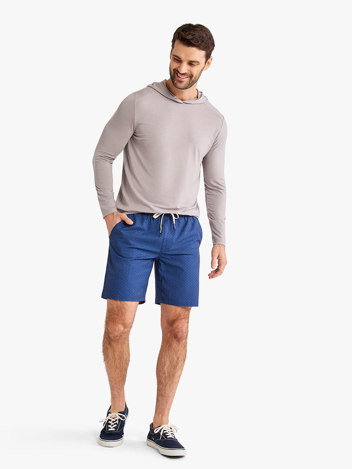 Man wearing gray long-sleeve hoodie and blue shorts with circle pattern design.