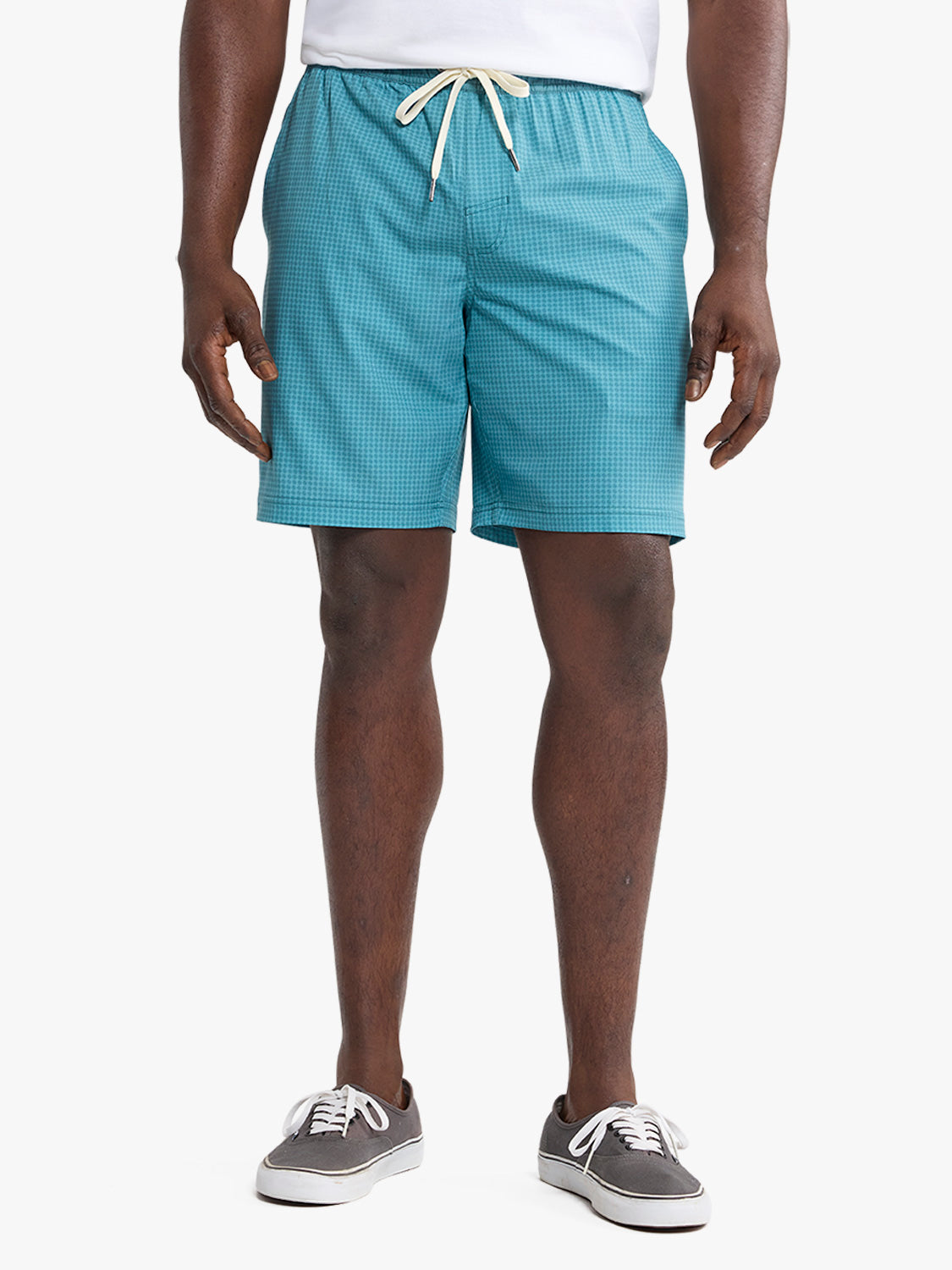 Man wearing turquoise geometric patterned shorts with cream drawstring and canvas sneakers.