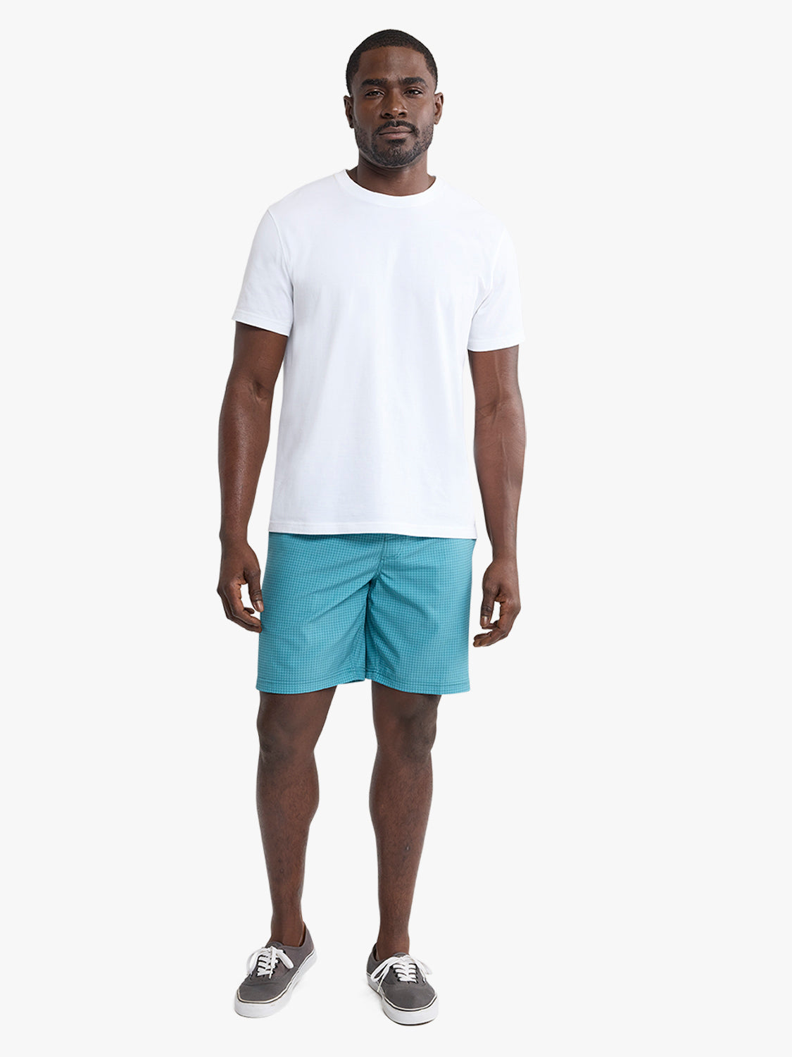 Man wearing white short-sleeve t-shirt and turquoise geometric patterned shorts with sneakers.