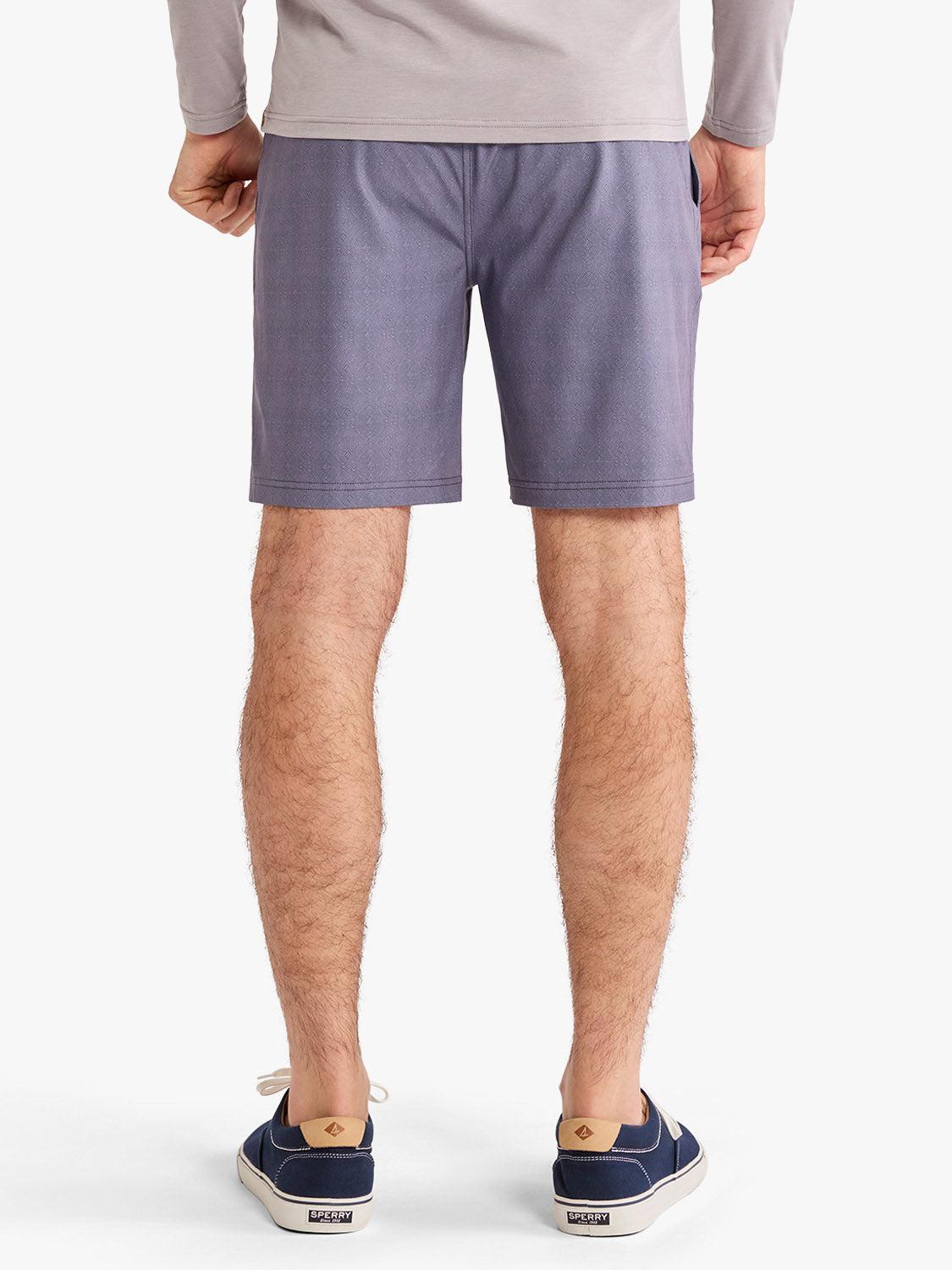 Man wearing dusk-colored shorts with a gray long-sleeved shirt and navy sneakers.