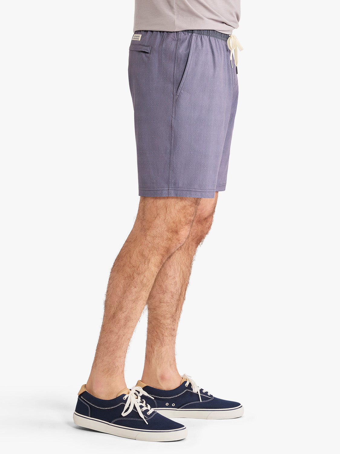 Man wearing dusk-colored shorts with elastic waistband and drawstring, paired with navy canvas sneakers.