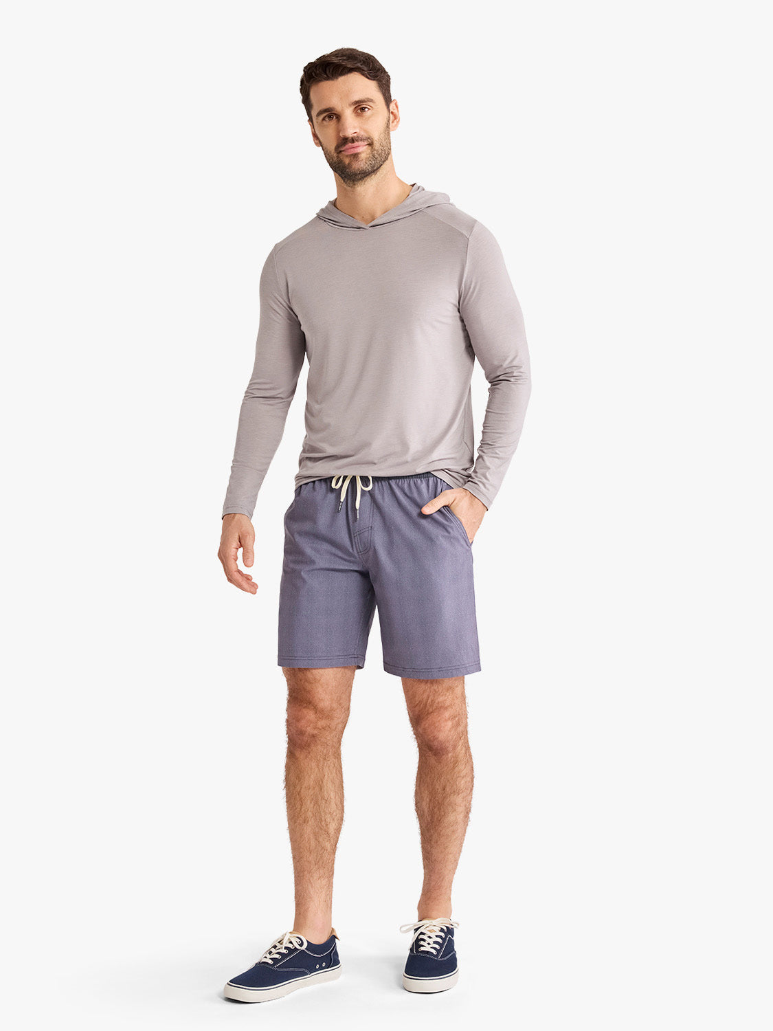 Man wearing a gray hooded long-sleeve shirt and purple drawstring shorts with sneakers.