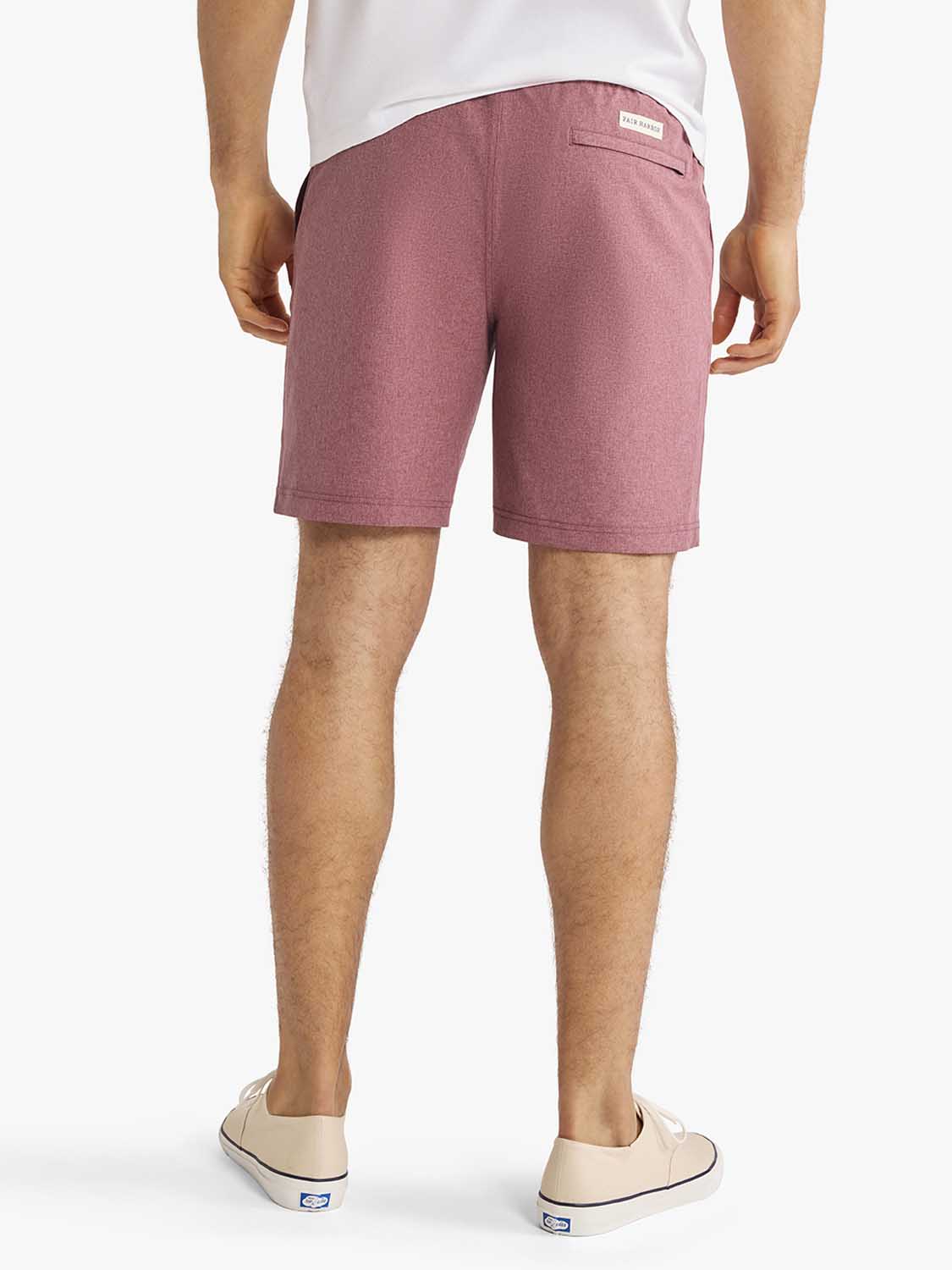 Man wearing burgundy shorts with a white t-shirt and cream canvas sneakers shown from behind.