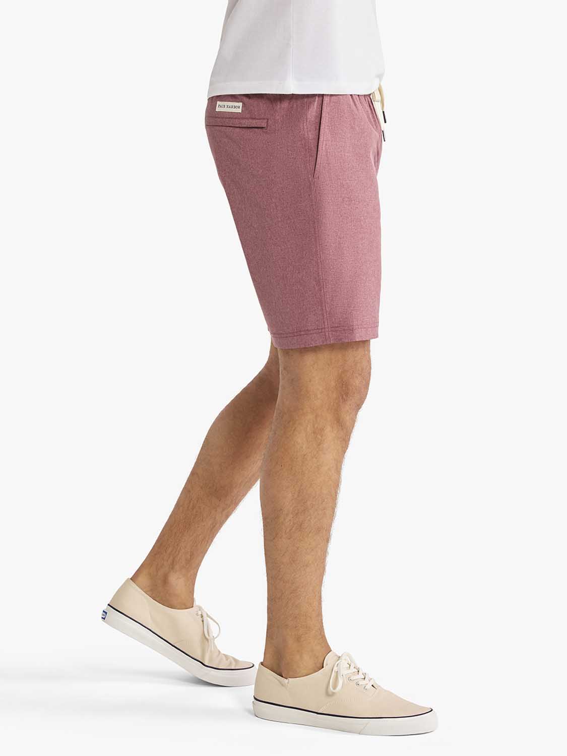 Man wearing burgundy shorts with a white shirt and cream canvas sneakers.