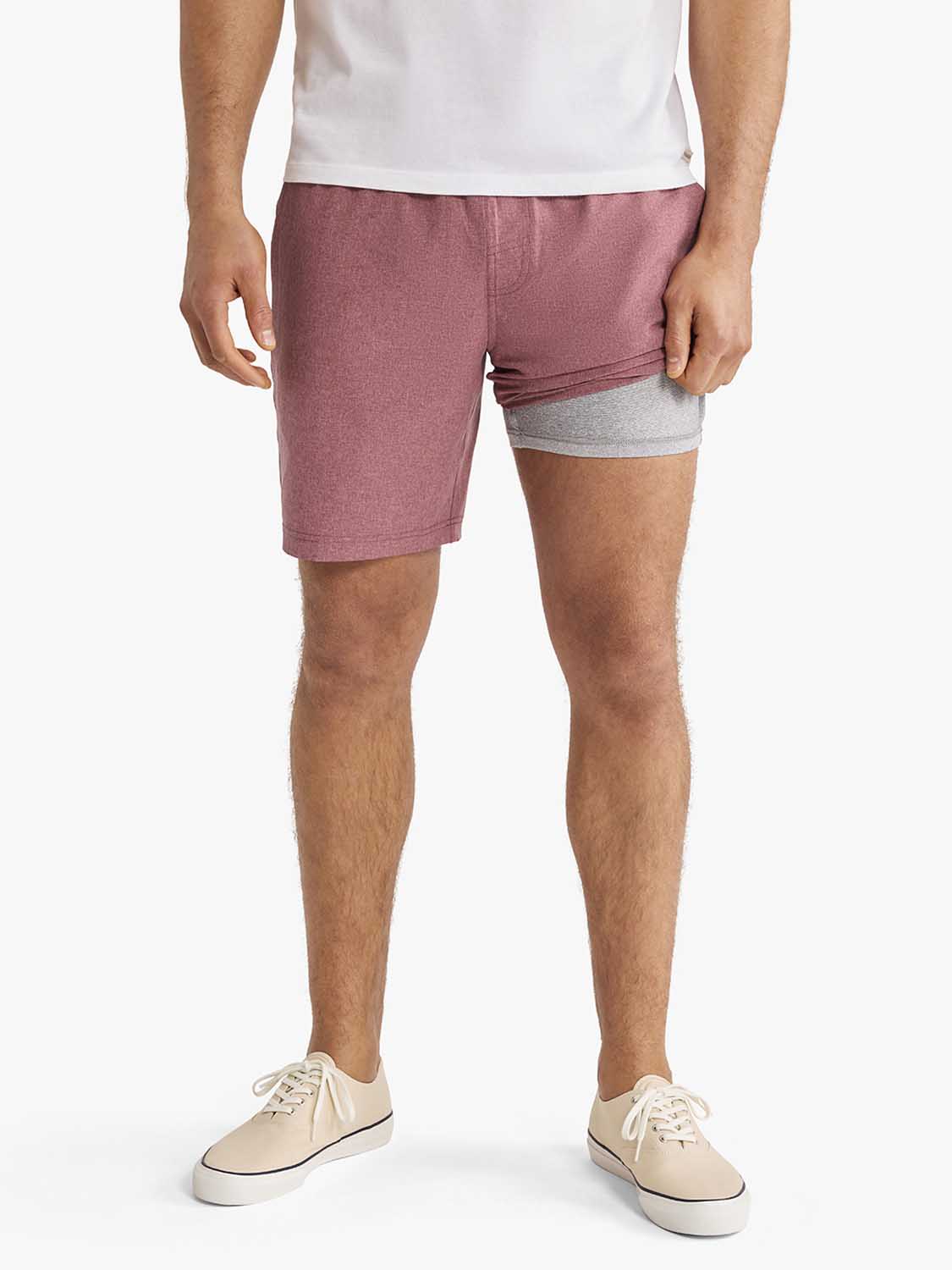 Man wearing burgundy shorts with gray waistband and white t-shirt standing against white background.