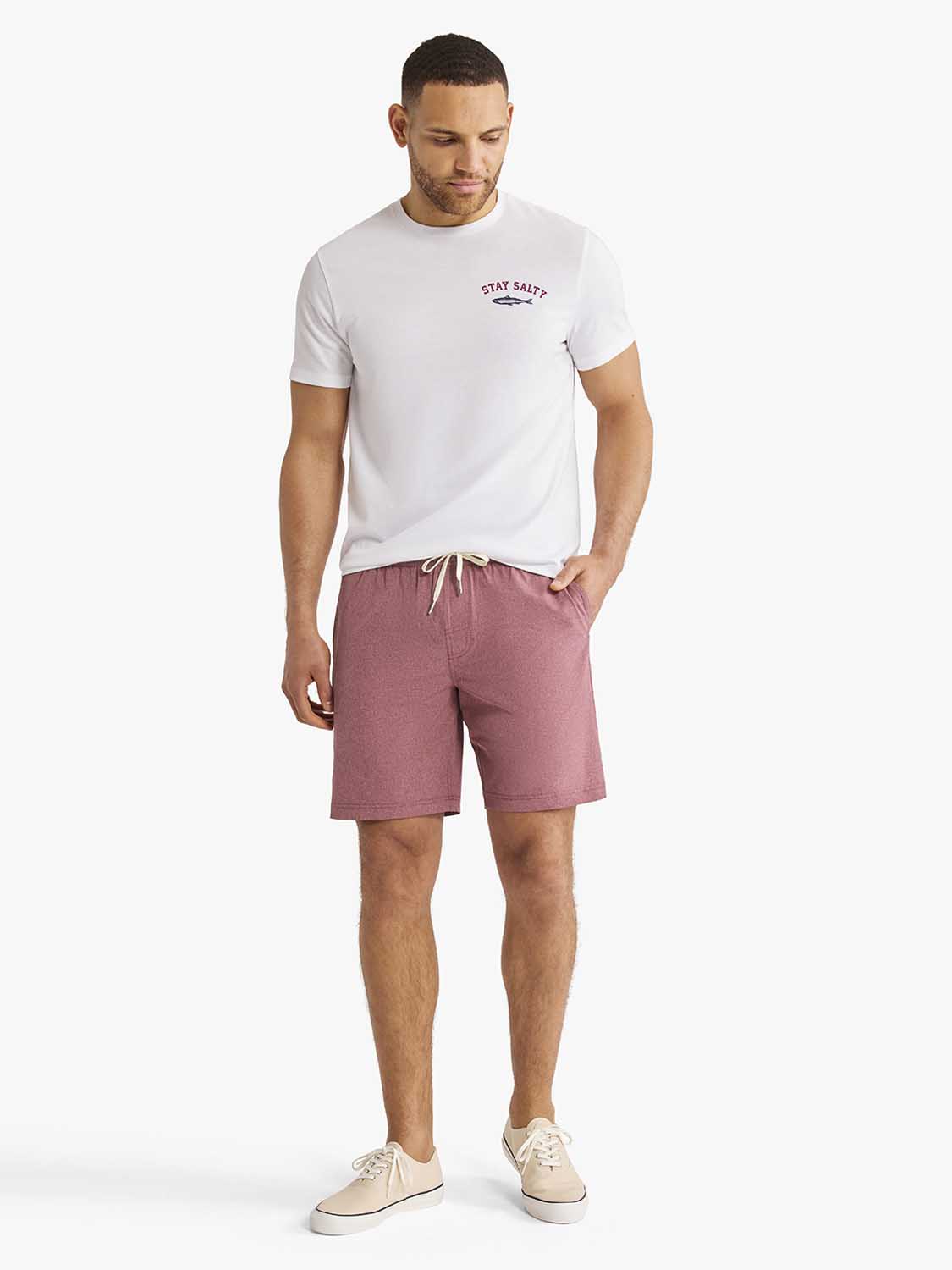 Man wearing white short-sleeve t-shirt with burgundy shorts and beige canvas sneakers.