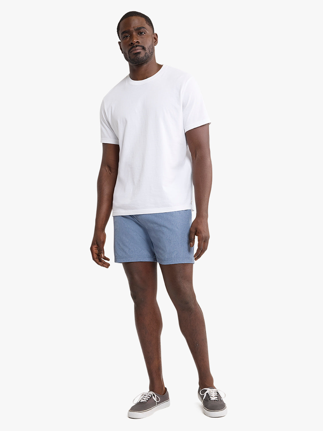 Man wearing a white short-sleeve t-shirt and blue denim shorts standing against a white background.