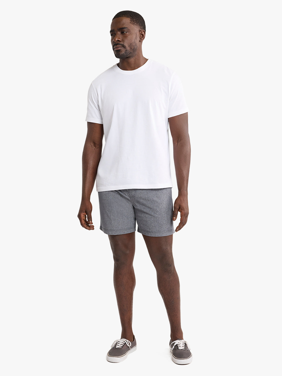 Man wearing a white short-sleeve t-shirt and grey shorts with canvas sneakers.