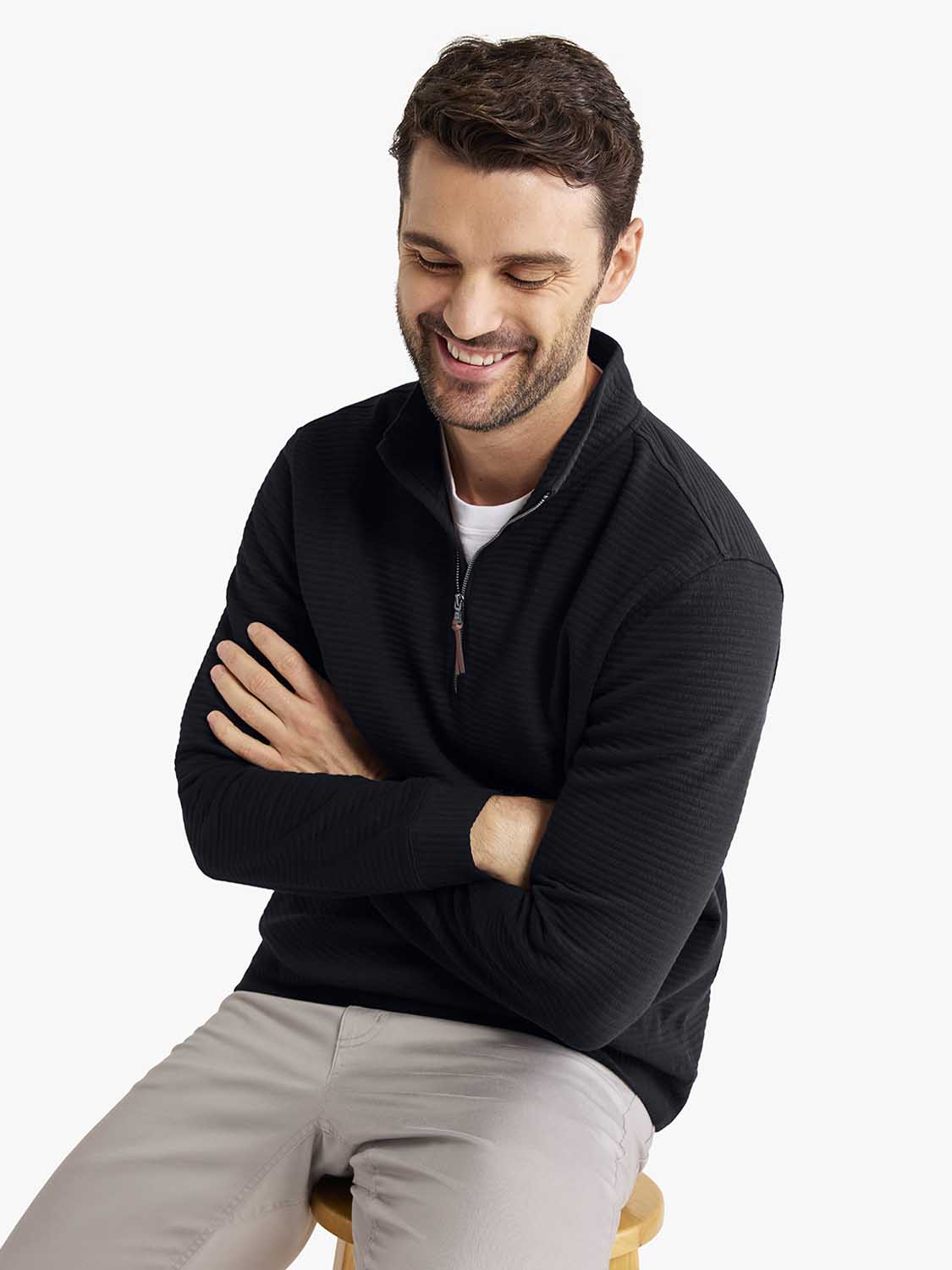 Man wearing black quarter zip pullover with textured fabric over white shirt and tan pants.