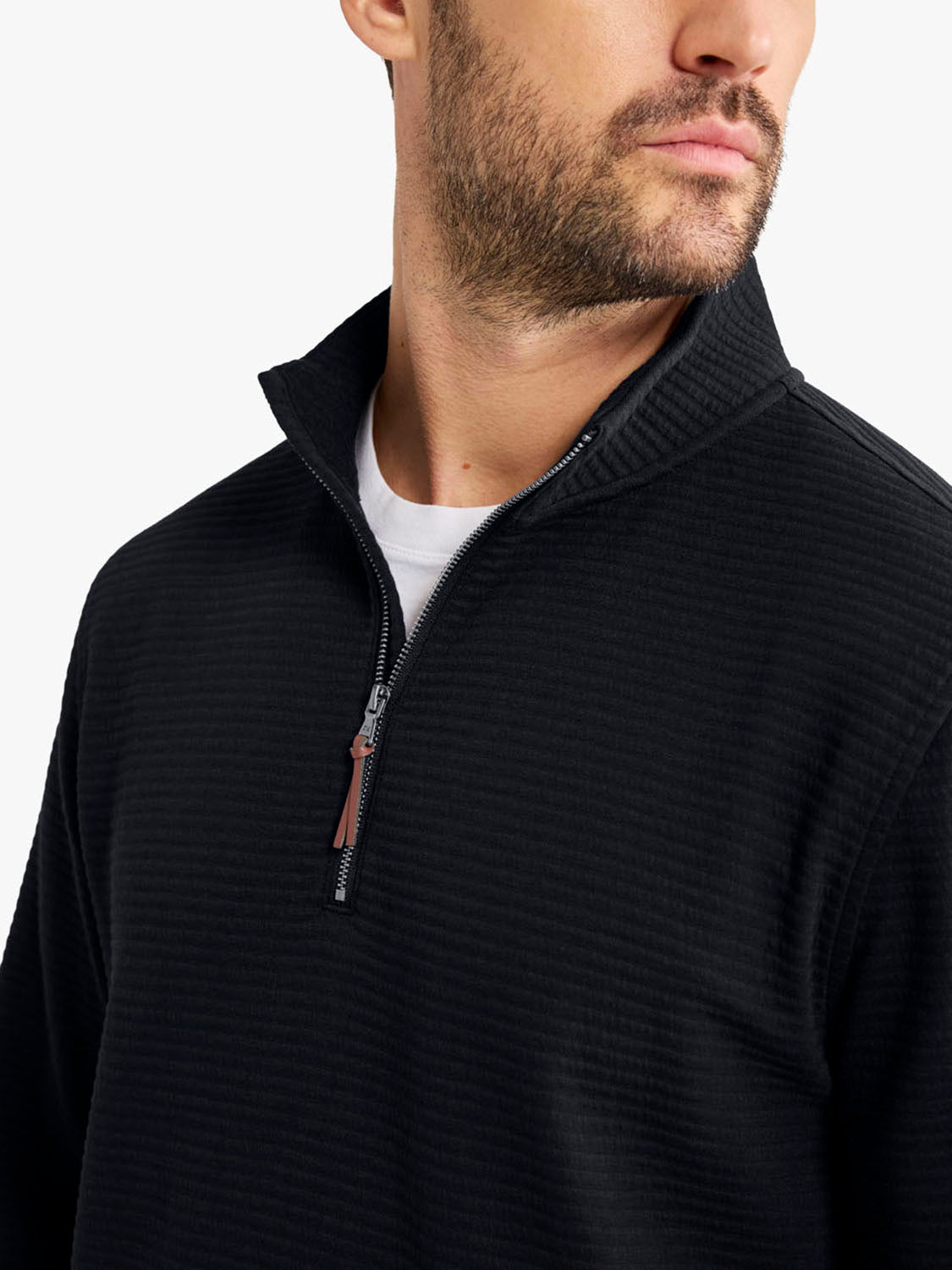 Man wearing a black quarter zip pullover with ribbed texture and a leather zipper pull.