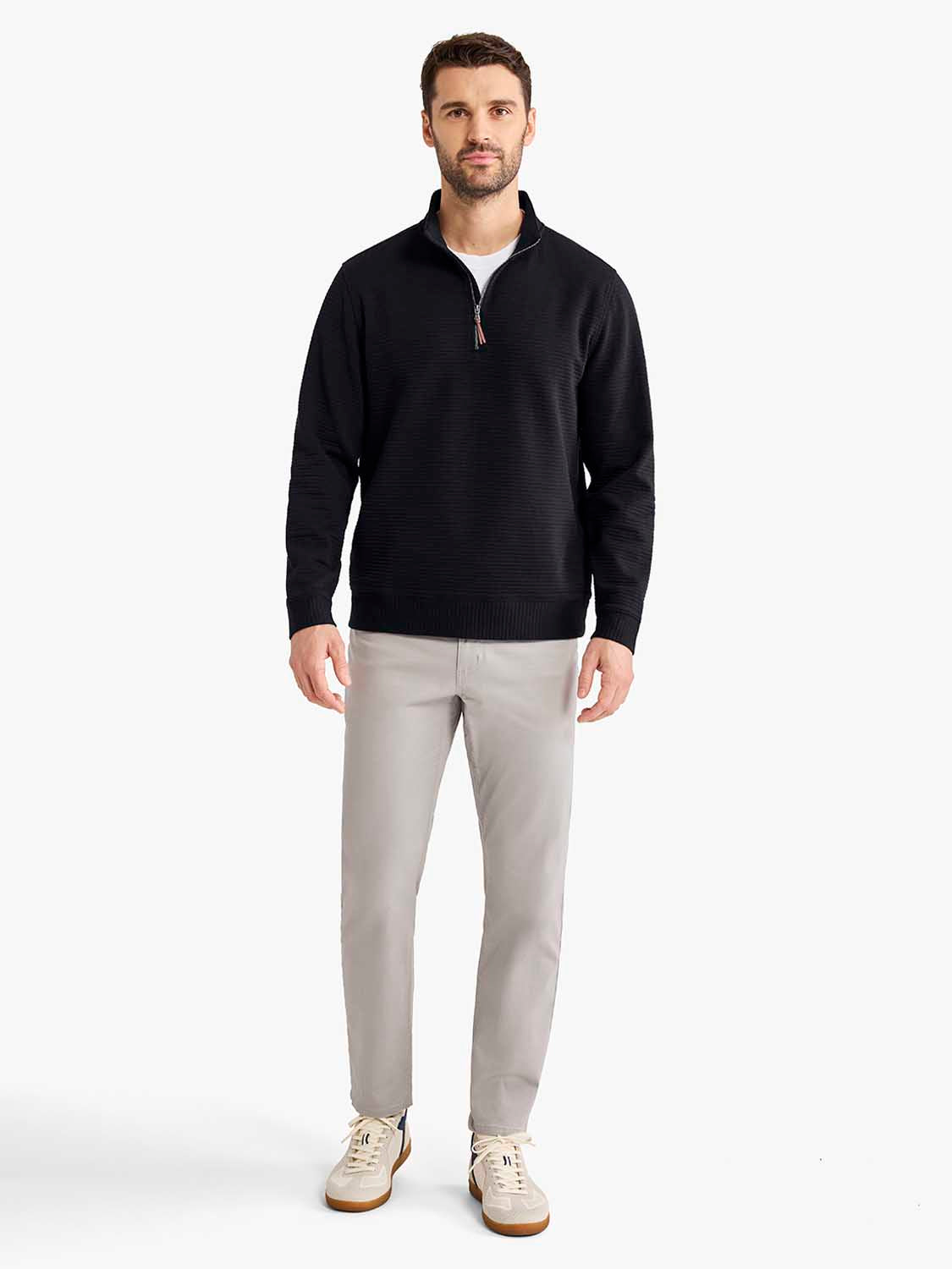 Man wearing black quarter zip pullover sweater with light gray pants and cream sneakers.