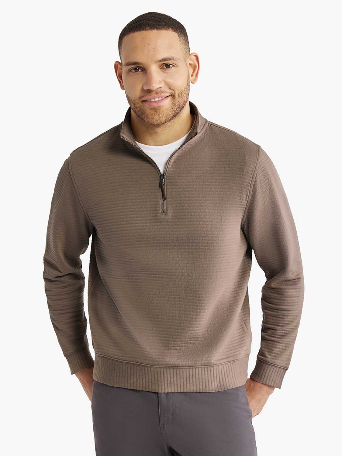 Man wearing a taupe quarter-zip pullover with long sleeves and ribbed cuffs over a white shirt.