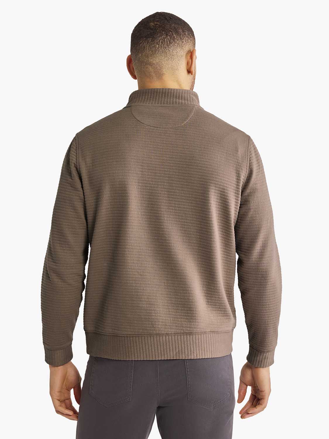 Man wearing a taupe quarter zip pullover sweater with ribbed texture and dark pants.