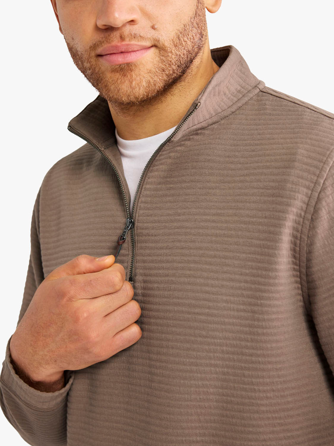 Man wearing a tan quarter zip pullover with a textured fabric and white undershirt visible.