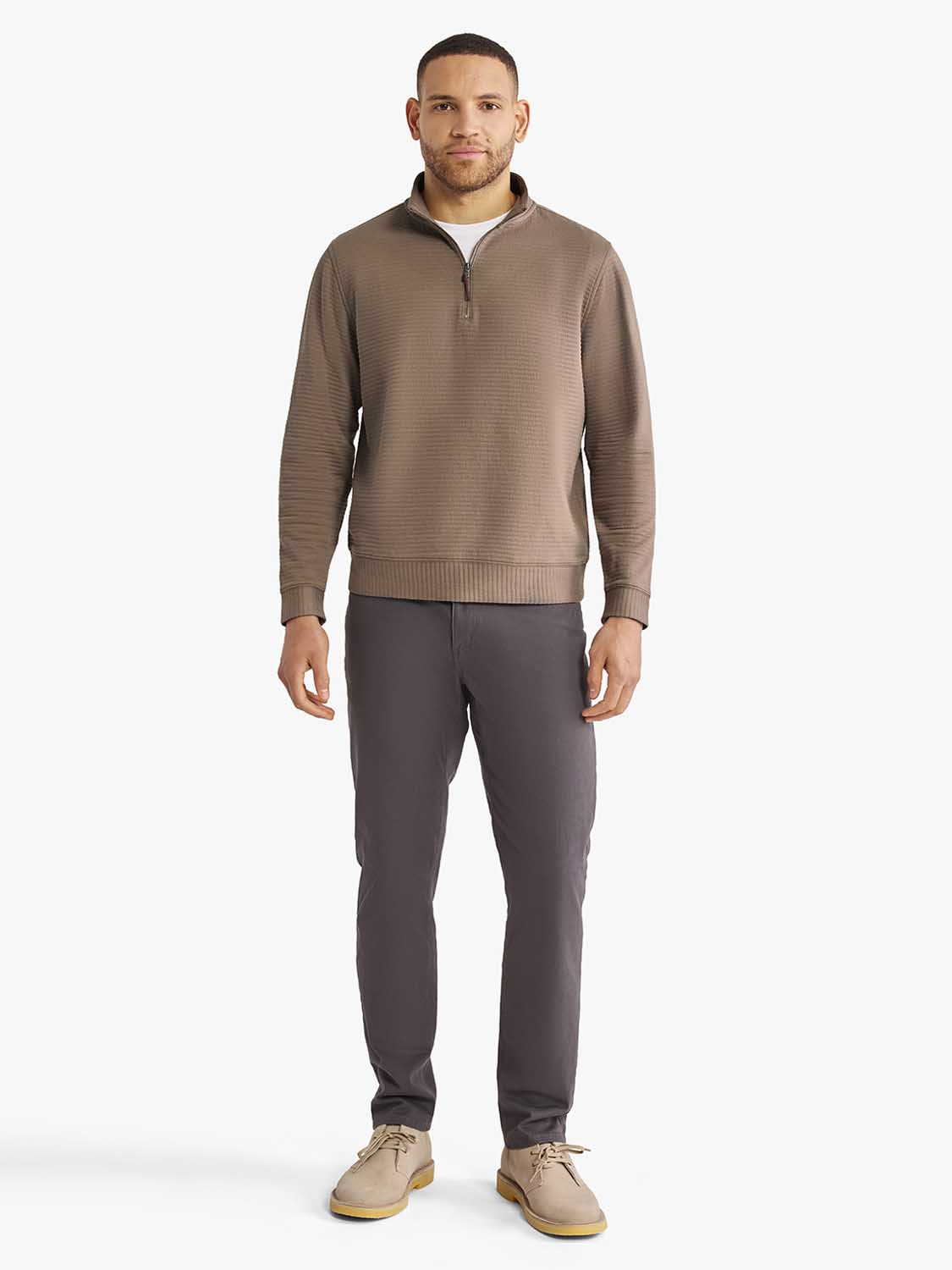 Man wearing a sandbar-colored quarter zip pullover with dark gray pants and tan boots.