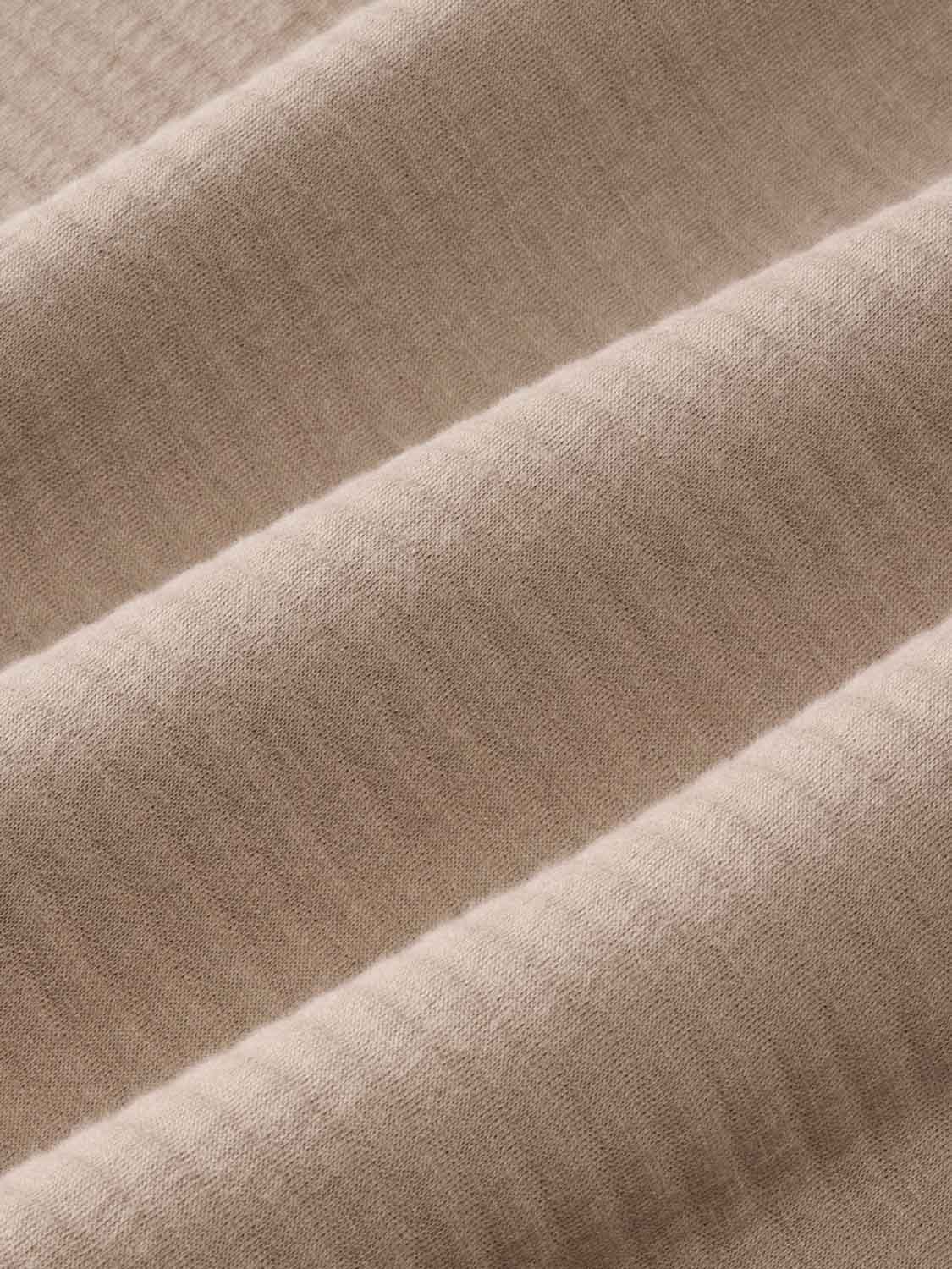 Close-up of sandbar-colored quarter zip fabric showing diagonal quilted seams and textured weave.
