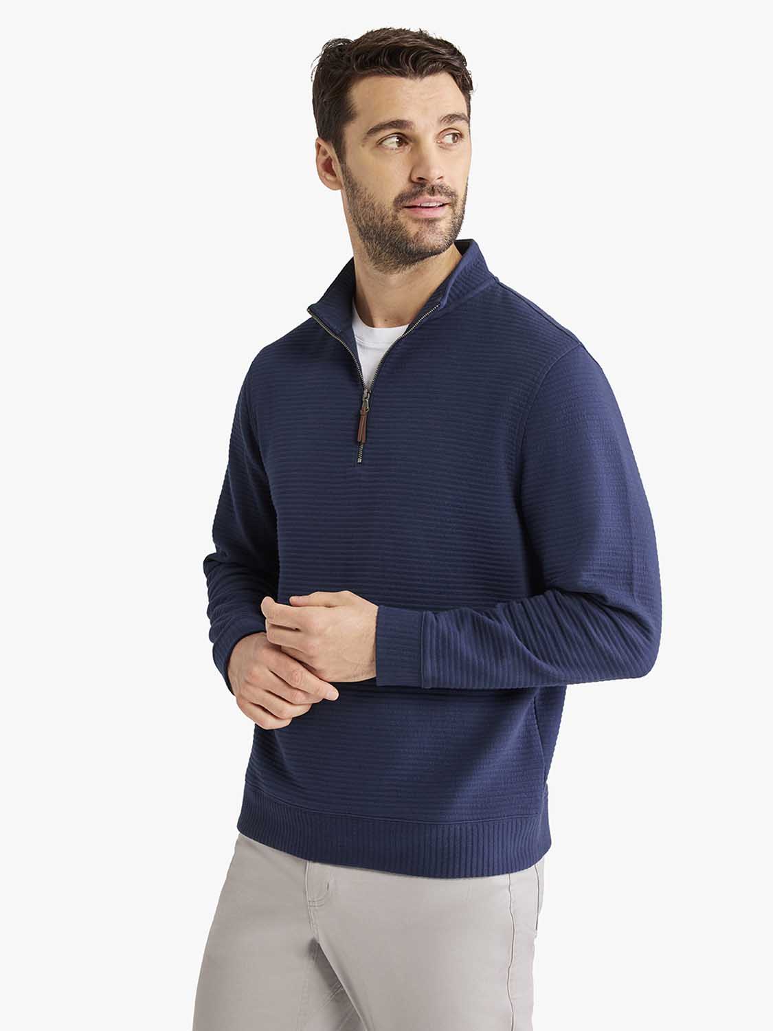 Man wearing a navy quarter zip pullover with textured knit fabric and brown zipper pull.
