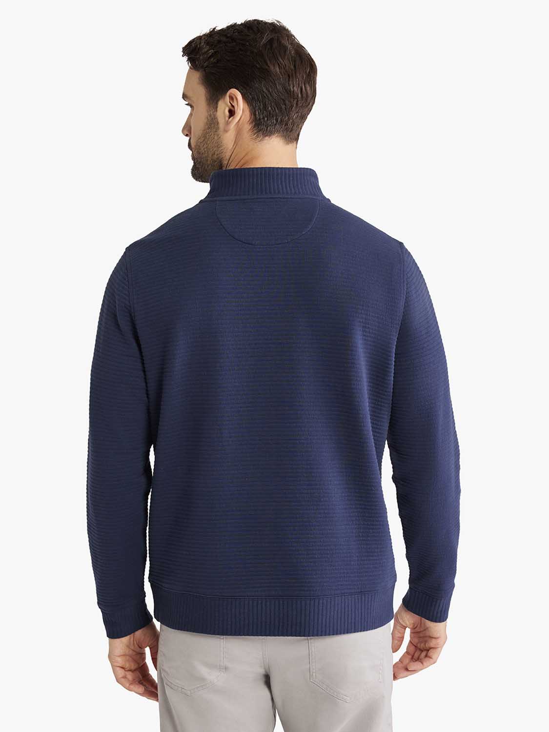 Man wearing navy quarter zip pullover with textured knit fabric and ribbed collar from back view.
