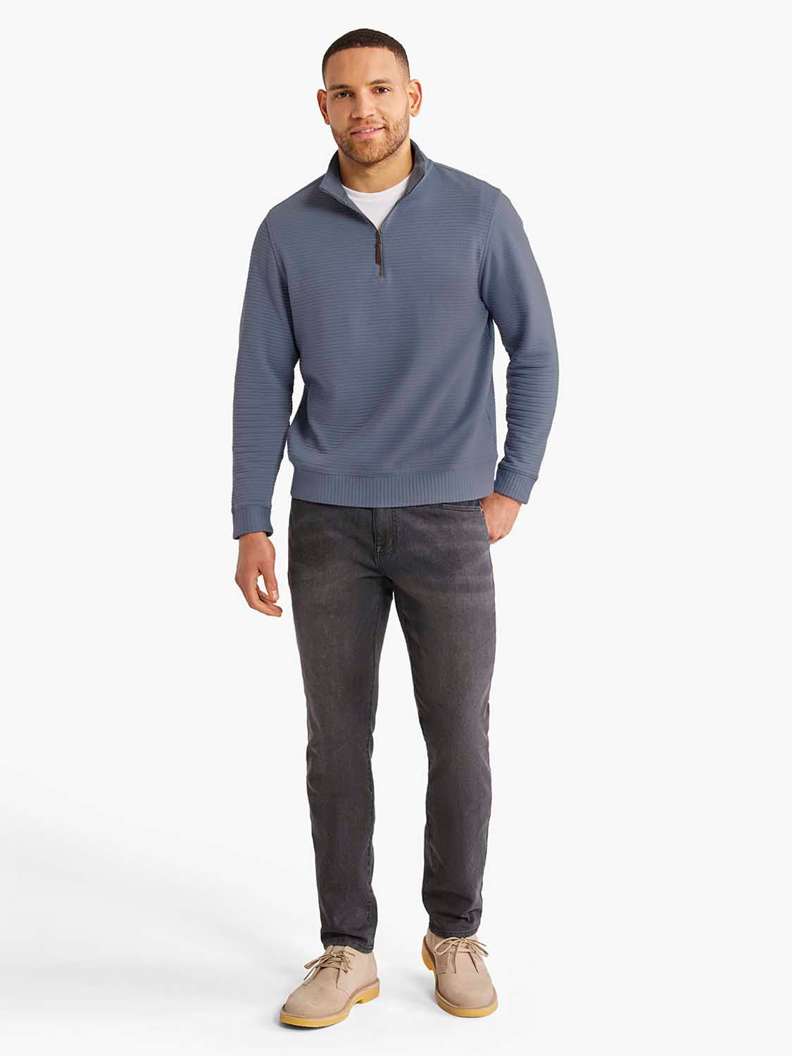 Man wearing a blue-gray quarter zip pullover with dark jeans and tan boots.