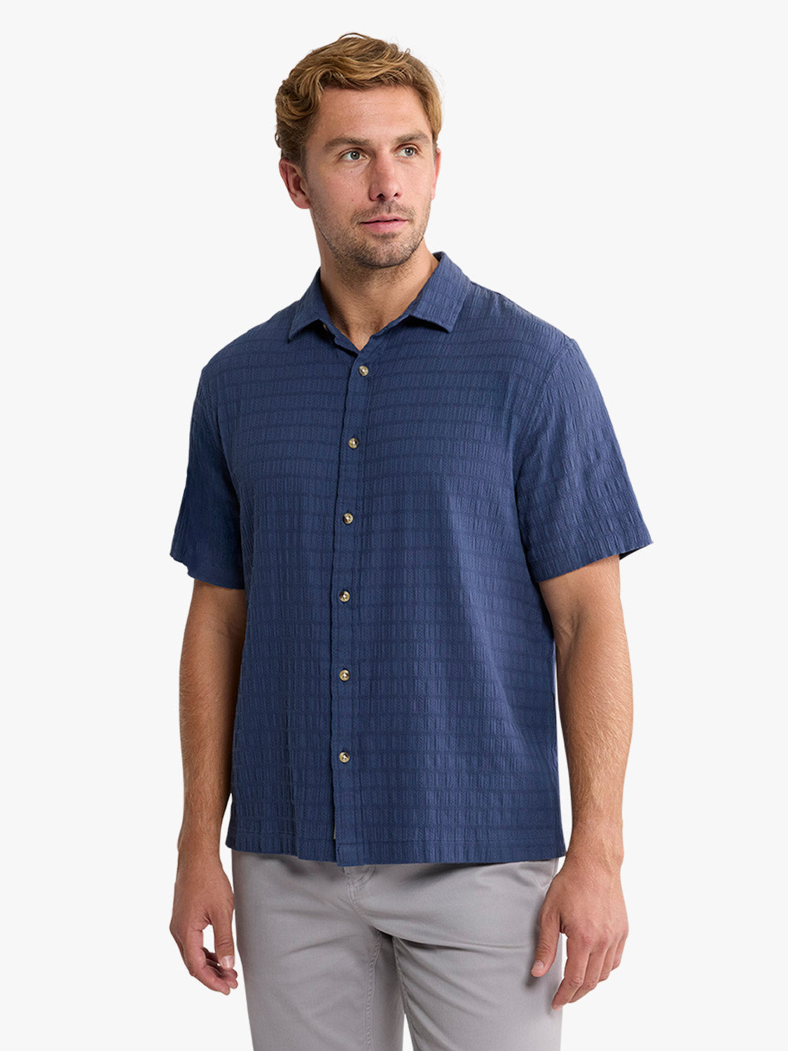 Man wearing a navy basket weave textured short-sleeve button-up shirt with tan buttons.