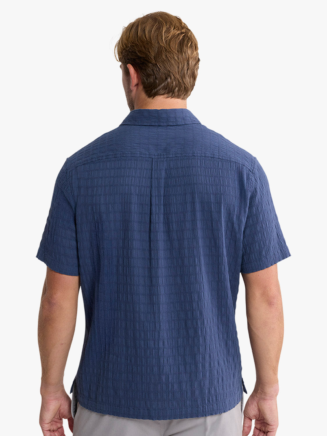 Man wearing navy blue short-sleeved shirt with textured basket weave pattern, shown from back.