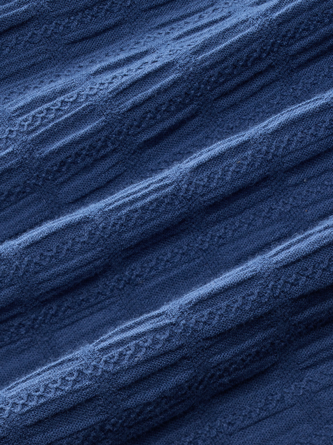 Navy blue fabric with a textured basket weave pattern showing diagonal folds and ridges.