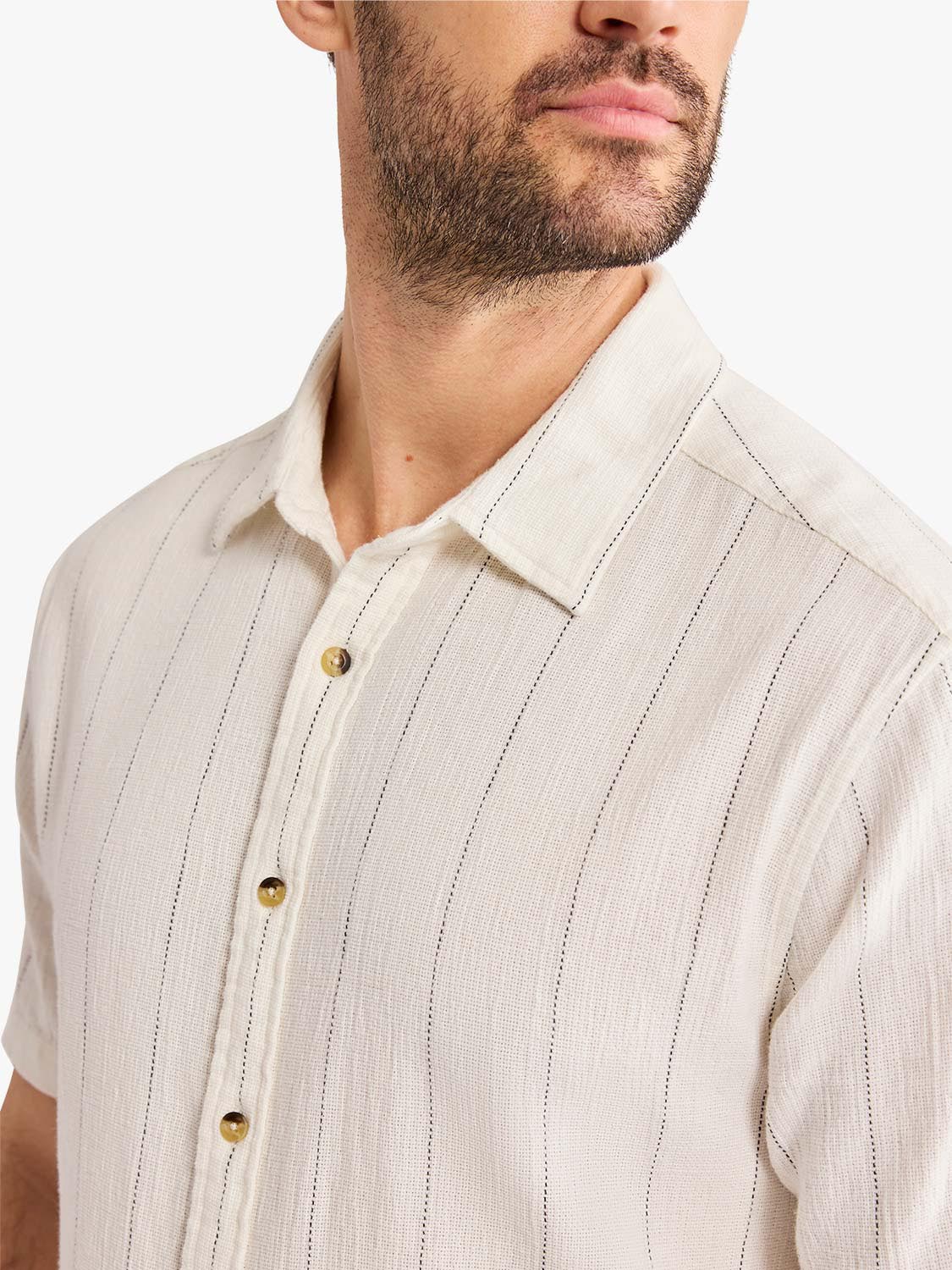 Man wearing a cream-colored textured shirt with vertical shell stripe pattern and gold buttons.