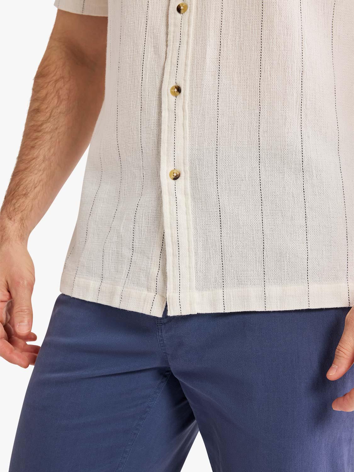 Beige textured shirt with vertical pinstripes and gold buttons worn over navy trousers.