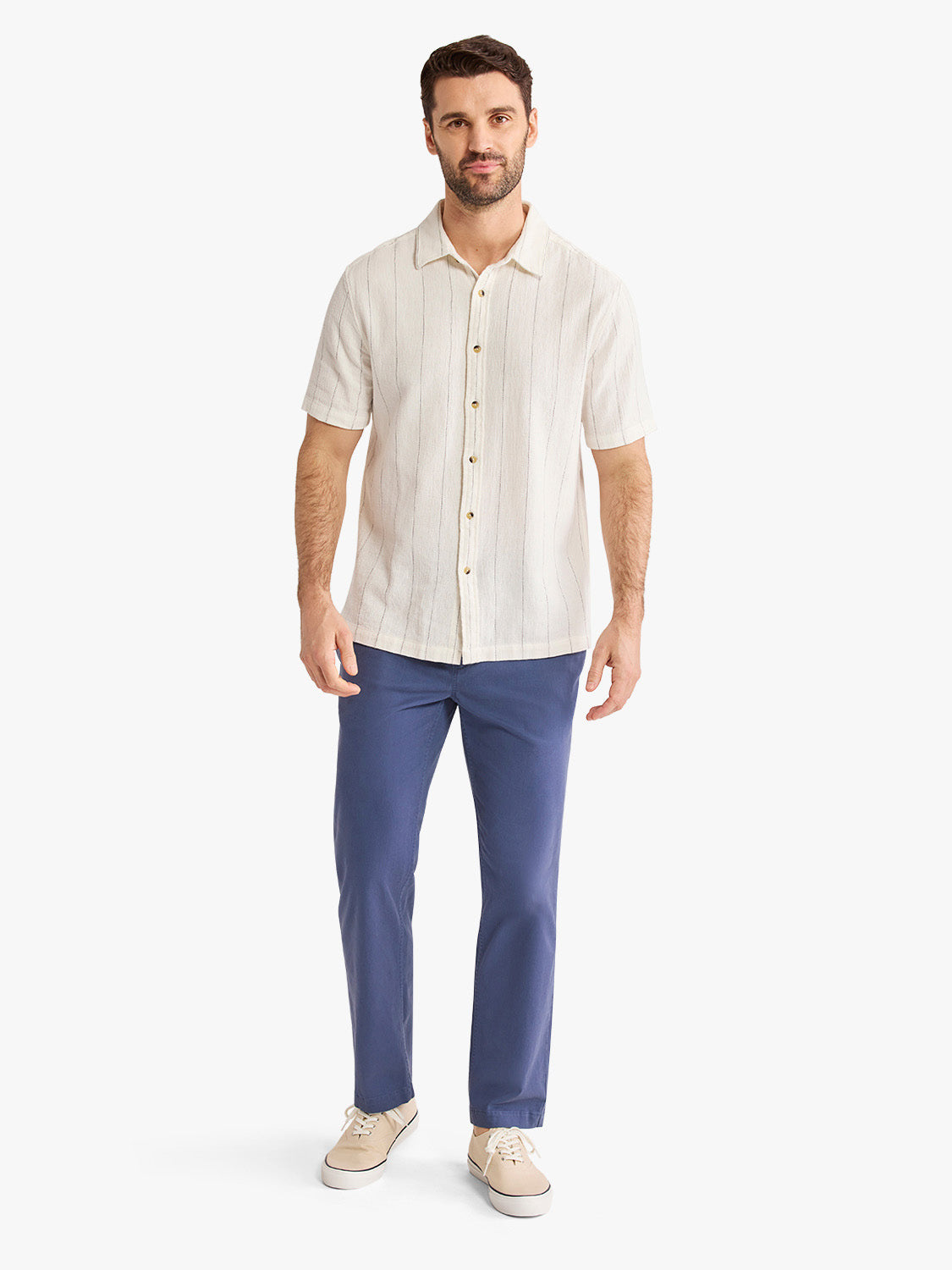Man wearing a cream short-sleeve button-up shirt with vertical stripe texture and navy blue pants.