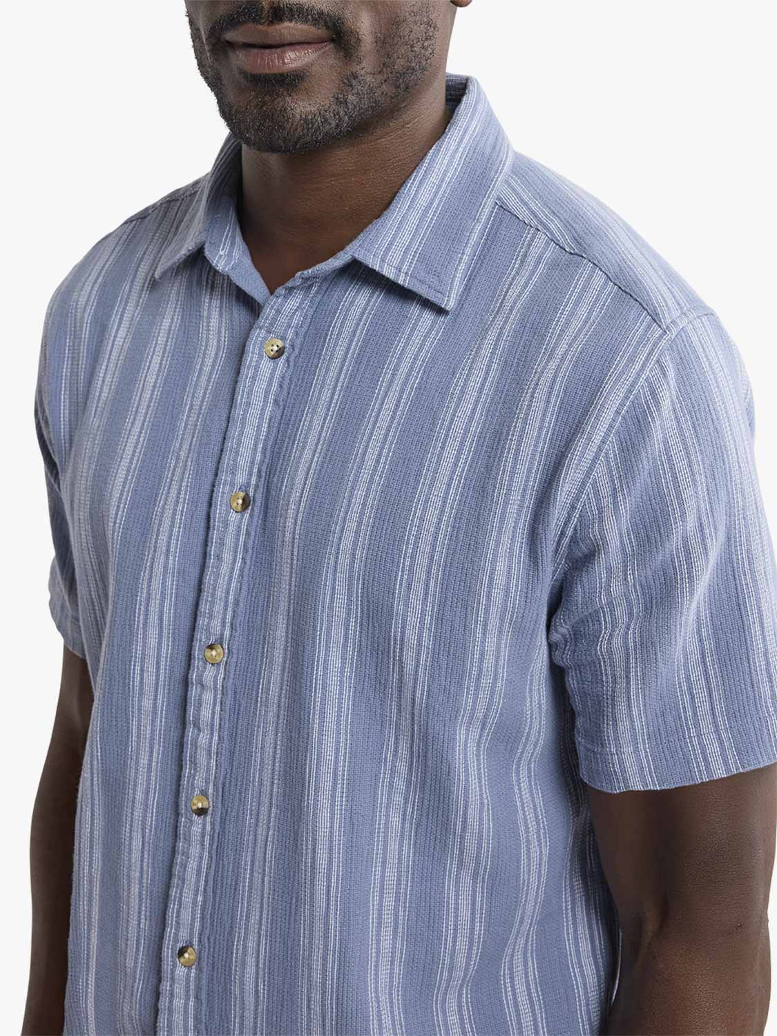 Man wearing a blue striped short-sleeve shirt with gold buttons and textured fabric.