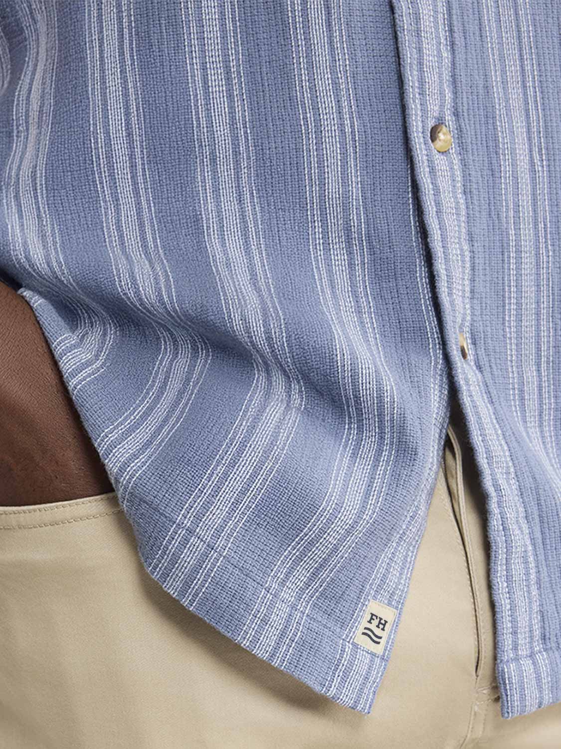 Blue and white striped textured shirt with button-up front and branded cuff label visible.