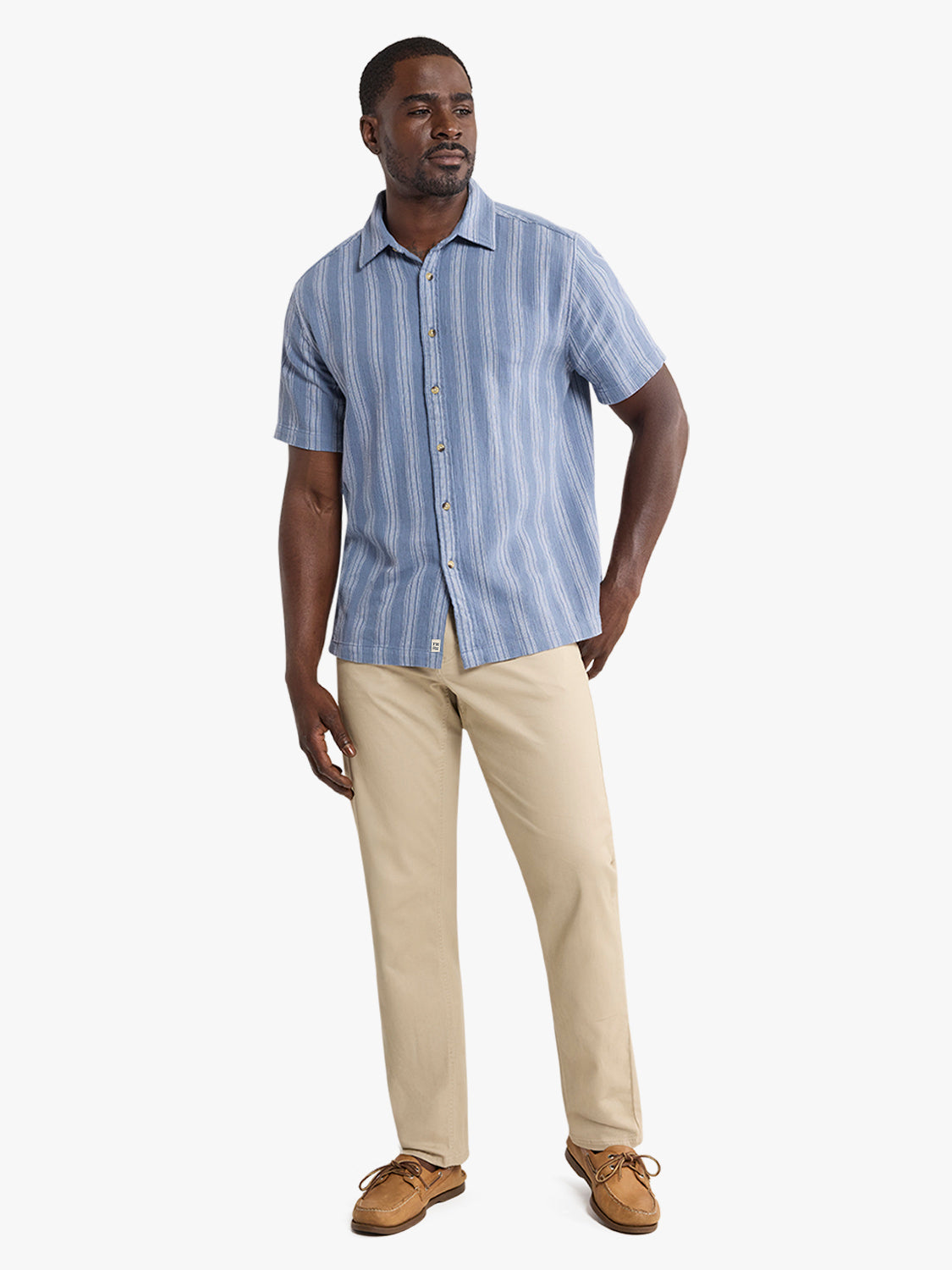 Man wearing a blue striped short-sleeve shirt with khaki pants and brown boat shoes.