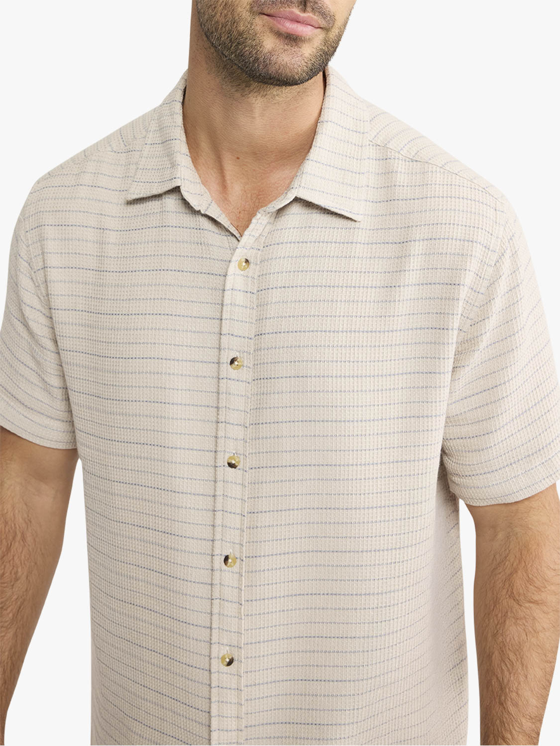 Man wearing a beige textured short-sleeve button-up shirt with horizontal striping and gold buttons.