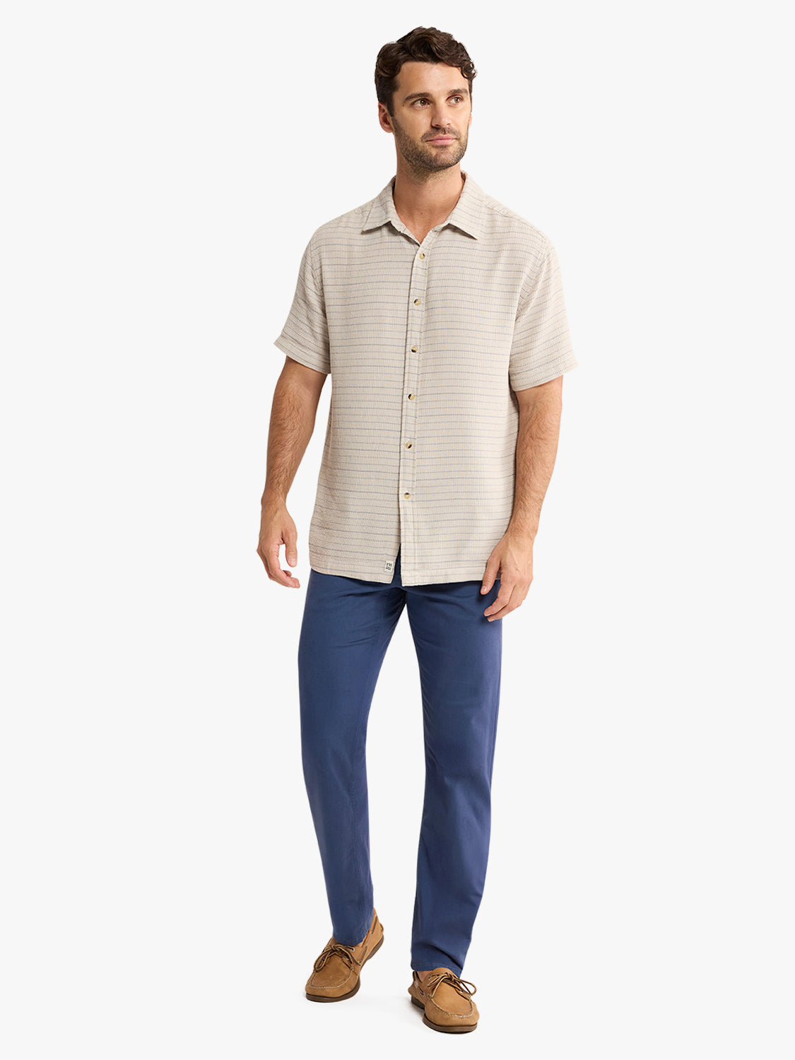 Man wearing a beige striped short-sleeve button-up shirt with navy pants and tan loafers.
