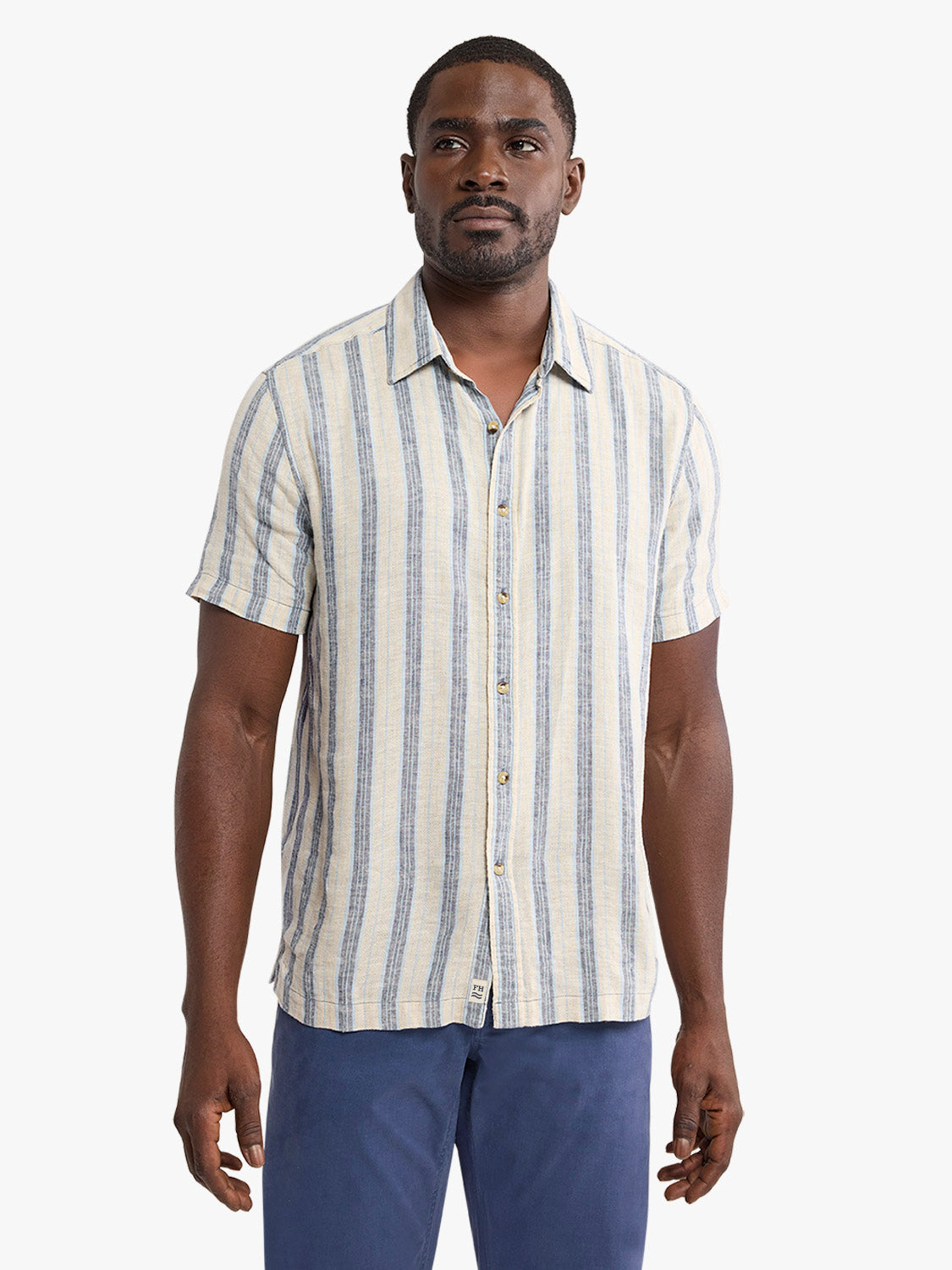 Man wearing a short-sleeved striped shirt with vertical blue and cream stripes and button front closure.