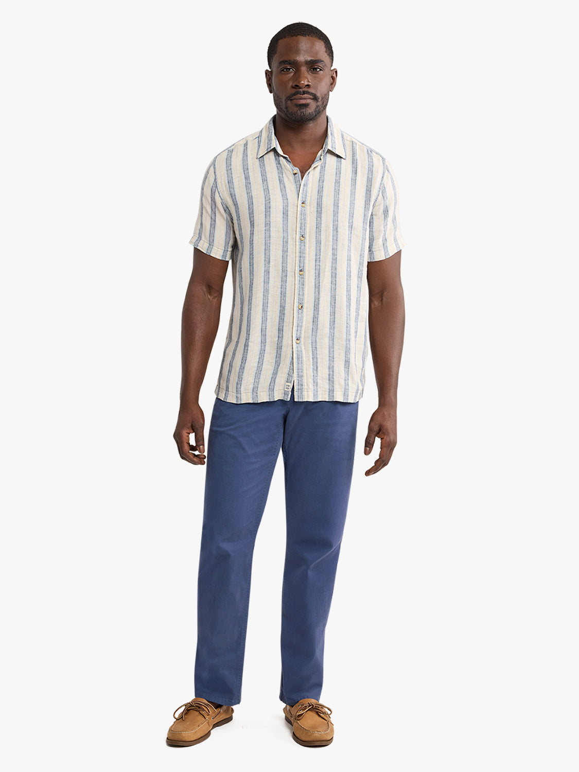Man wearing a short-sleeved striped shirt in cream and blue with dark blue pants and brown shoes.