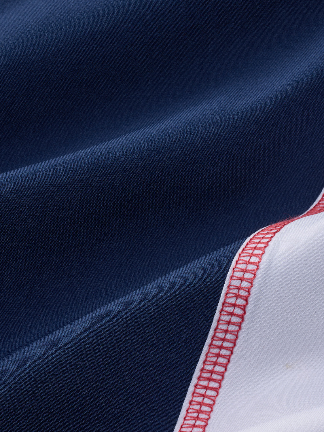 Navy board short with white and red sail panel detail and geometric stitching pattern visible.