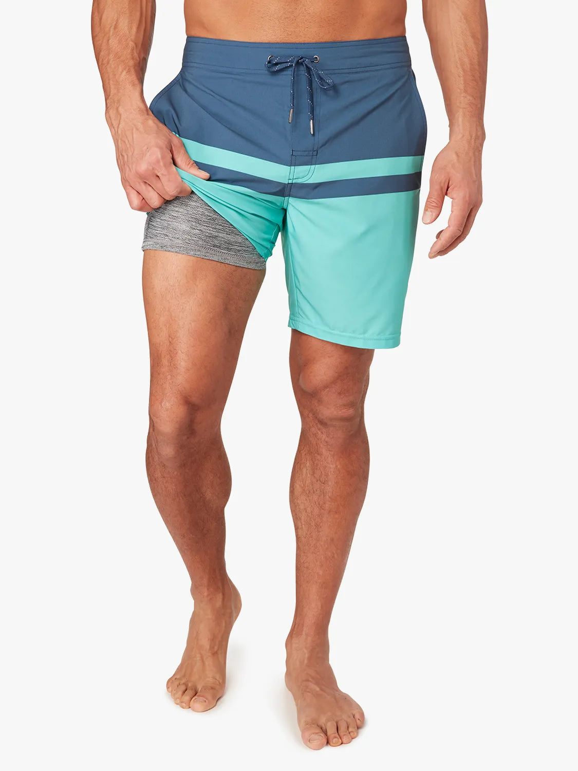 Person wearing a pair of navy blue and teal color blocked ozone board shorts on a white background, showing the liner view. 