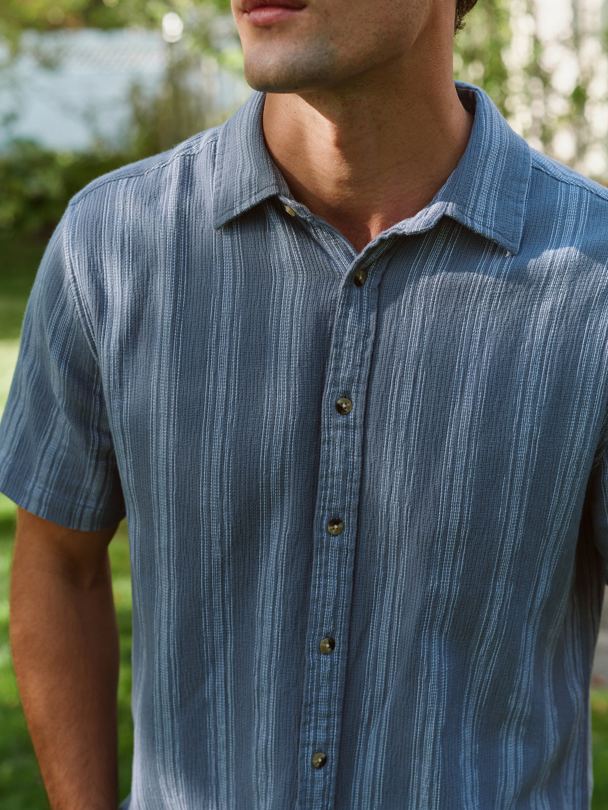 Man wearing a blue striped short-sleeve button-up shirt with a textured fabric outdoors.