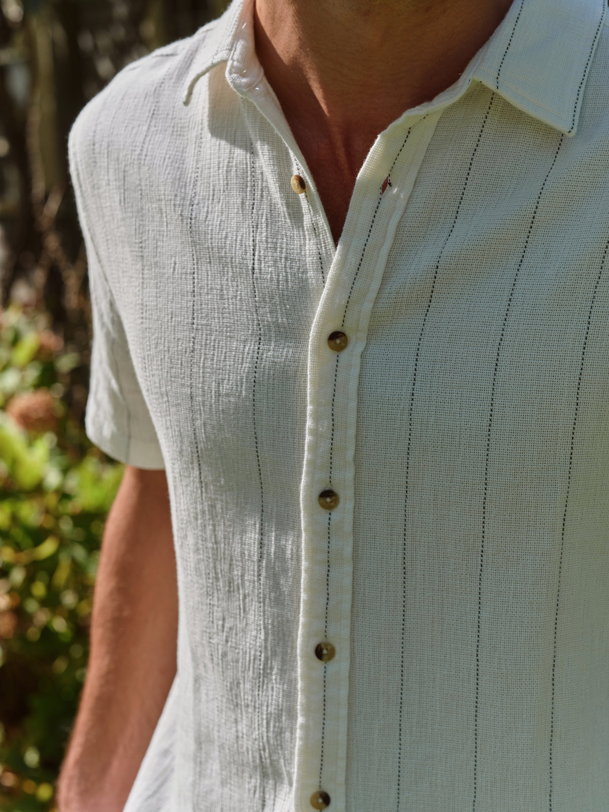 Man wearing a light blue textured short-sleeve button-up shirt with vertical pinstripe detailing and brown buttons.