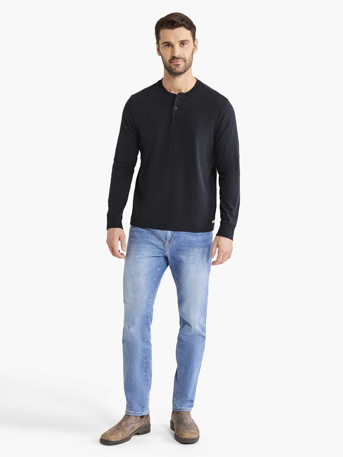 Man wearing a black long-sleeve henley shirt with blue jeans and brown boots.