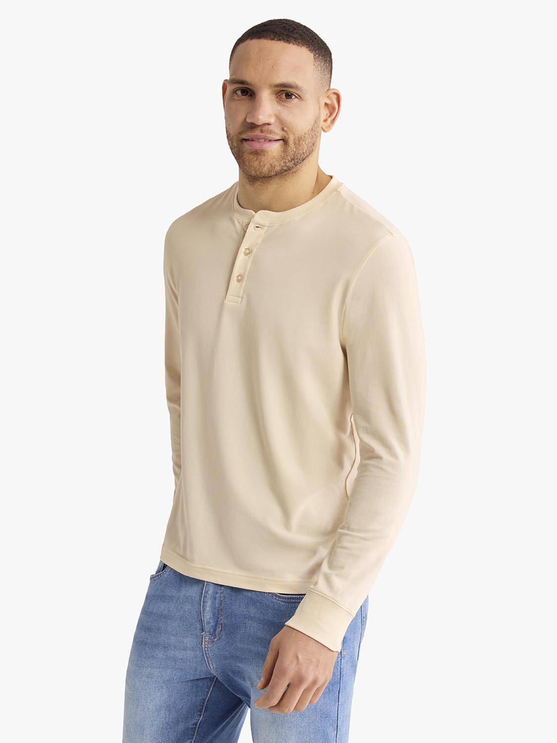 Man wearing a cream-colored long-sleeve henley shirt with button placket and blue jeans.