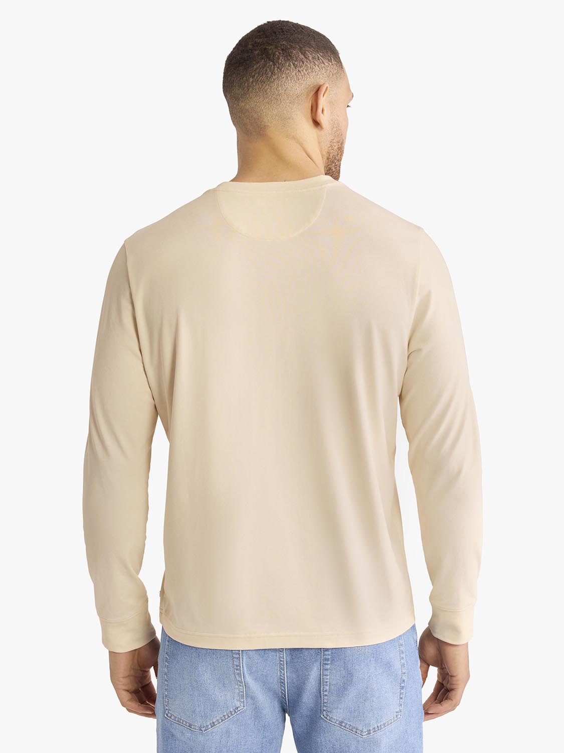Man wearing a cream-colored long-sleeve henley shirt with blue jeans, shown from behind.