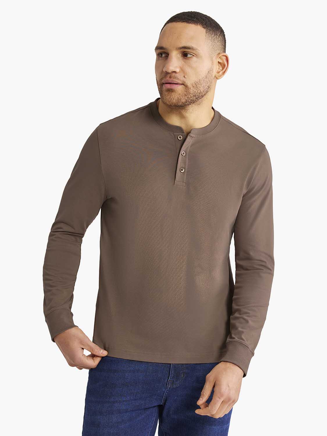 Man wearing a taupe long-sleeve henley shirt with button placket and dark jeans.