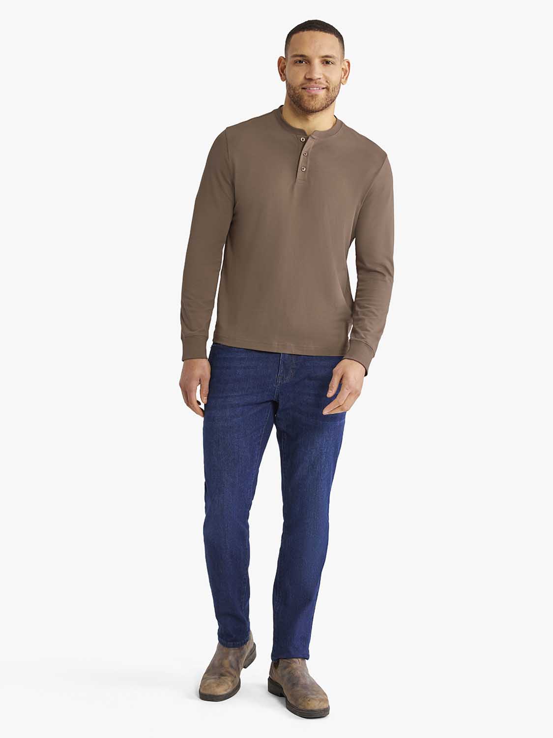 Man wearing a tan henley shirt with button placket and dark blue jeans.