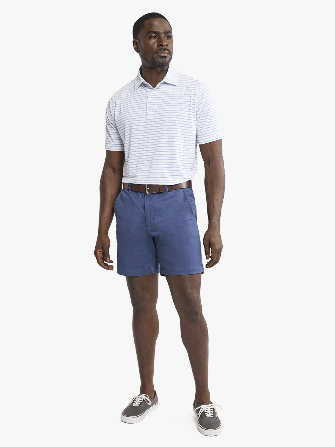 Man wearing a coastal blue striped polo shirt with navy shorts and gray sneakers.