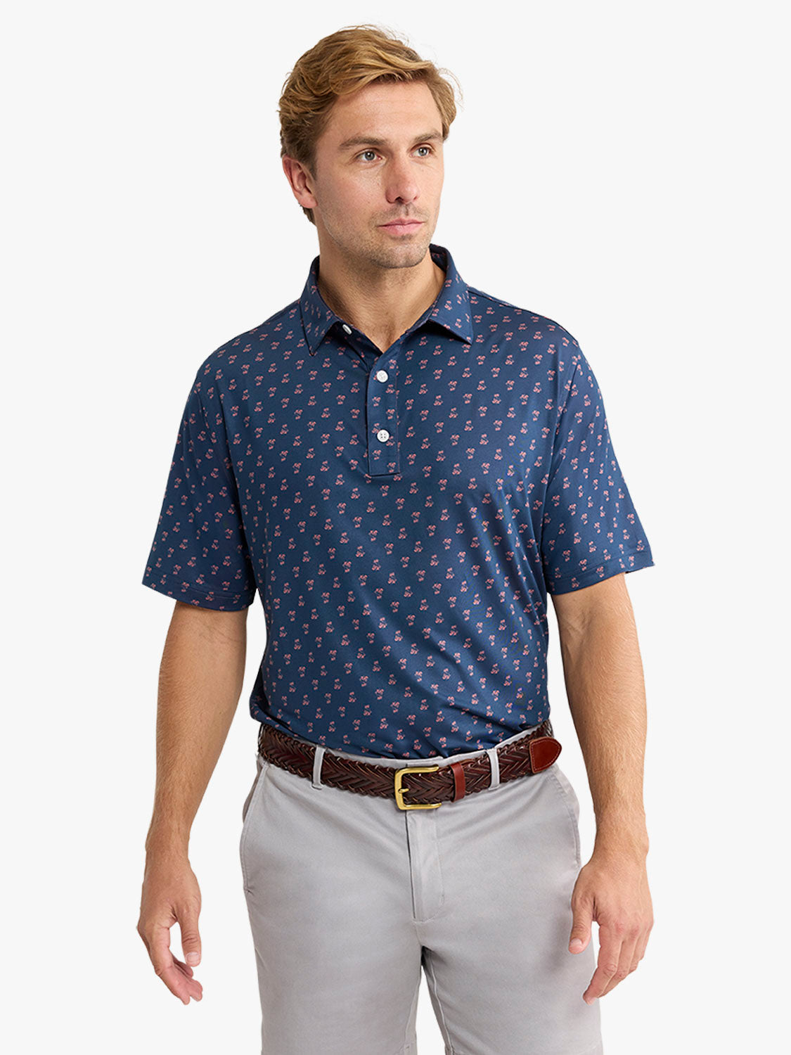Man wearing navy short-sleeved polo with small red pattern, paired with light gray pants and brown belt.