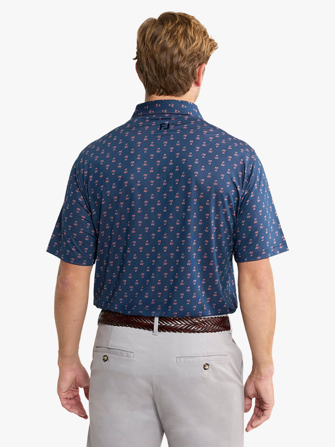 Man wearing navy polo shirt with small red pattern and light gray pants with brown woven belt.
