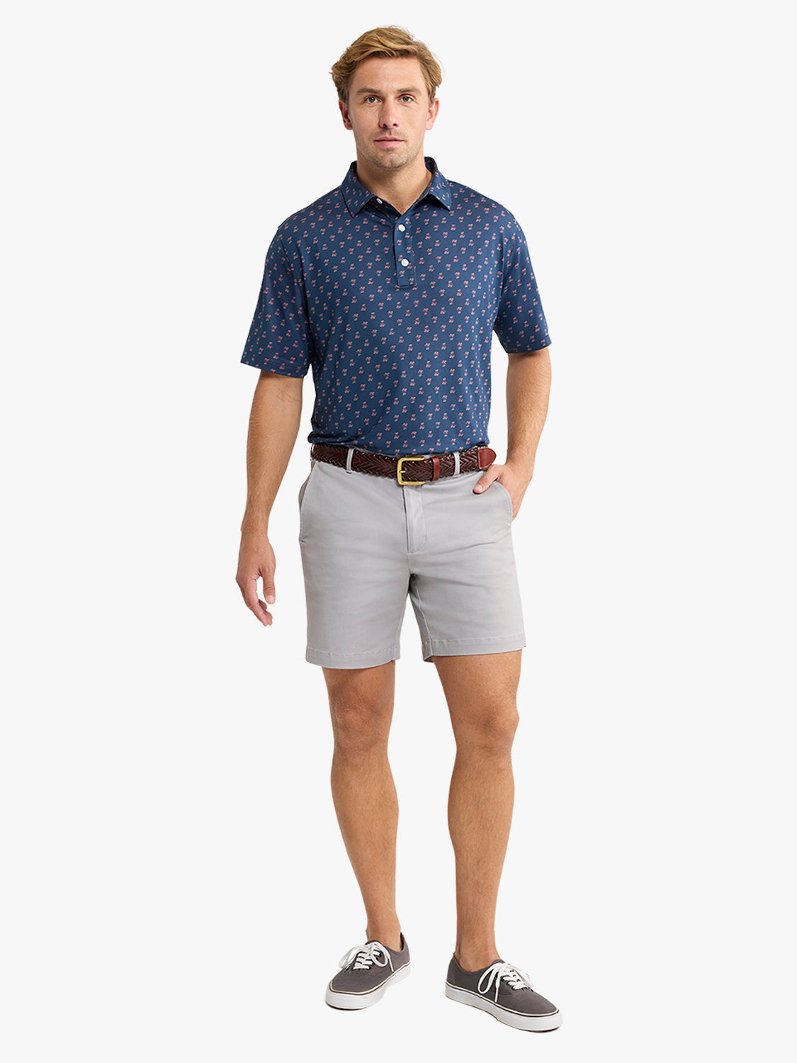 Man wearing a navy short-sleeve polo shirt with small pattern, light gray shorts, brown belt, and gray sneakers.